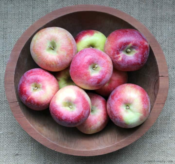 overhead shot of a wooden bowl full of apples on top of a burlap table cloth