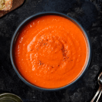 overhead shot of 3-ingredient tomato lentil soup in a dark bowl on top of a slate board