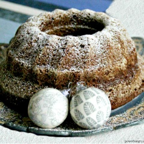 chickpea flour gingerbread bundt cake on a serving plate with some Christmas ornaments on the plate for decoration.