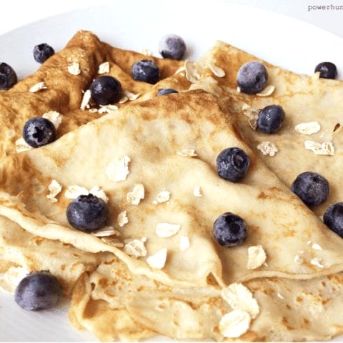 flourless blender oat crepes on a white plate with blueberries