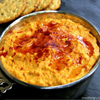 roasted carrot hummus in a decorative silver bowl with crackers in the background