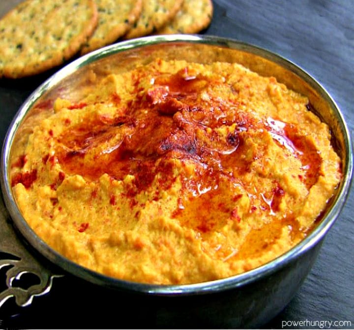 roasted carrot hummus in a decorative silver bowl with crackers in the background