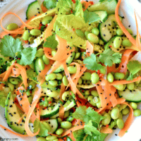 asian edamame carrot salad in a white bowl, sprinkled with black sesame seeds