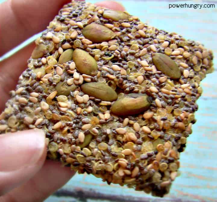 close-up of a hand holding a quinoa cracker with various seeds