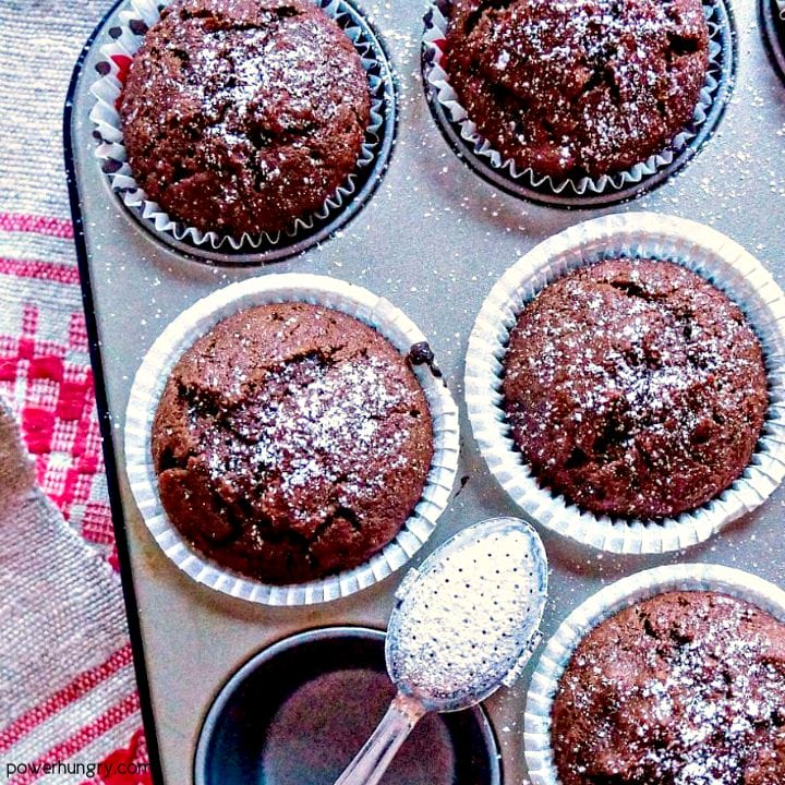vegan and grain-free chocolate chickpea flour muffins in a muffin tin, sprinkled with powdered sugar