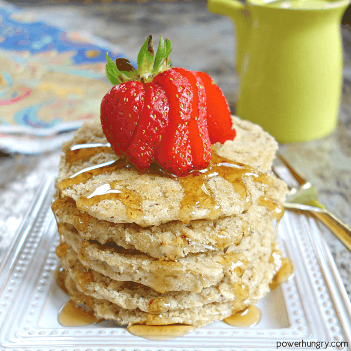 stack of vegan oat pancakes on a square white plate with a slied strawberry on top