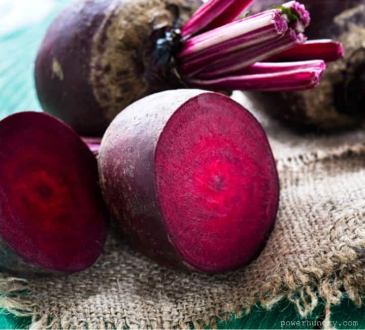 fresh raw beets, with one slice in half, atop a piece of burlap