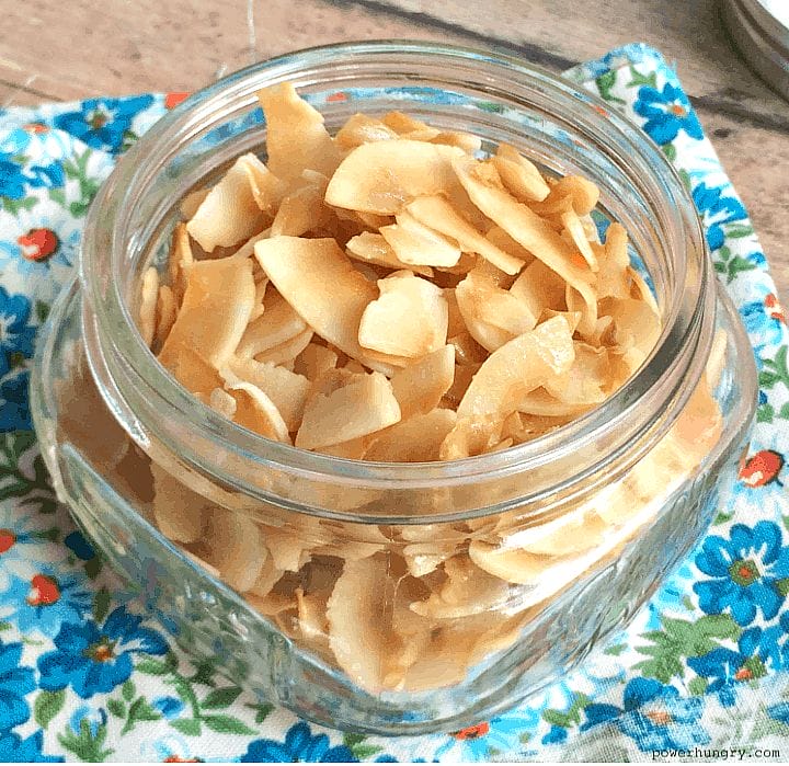 baked coconut chips in a glass jar on a floral napkin