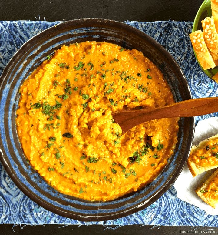 red lentil dal spread in a blue bowl with a wooden spoon