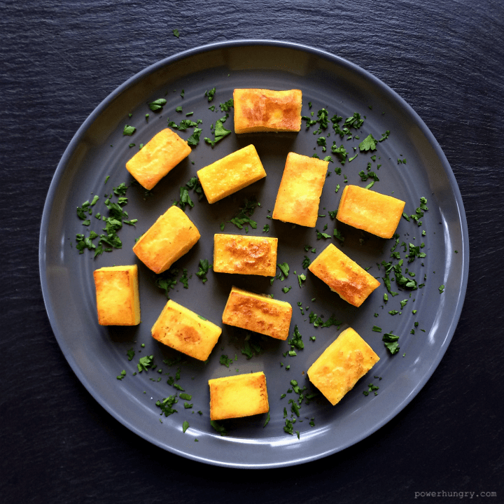 chickpea flour tofu cubes on a grey plate with chopped herbs