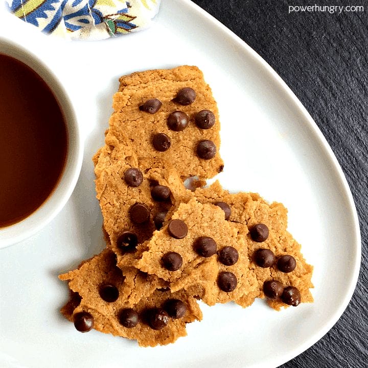 pieces of vegan chocolate chip cookie brittle on a white plate with a cup of coffee alongside