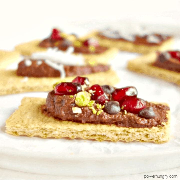 brownie batter hummus spread on graham crackers and topped with pomegranate seeds and chopped pistachios