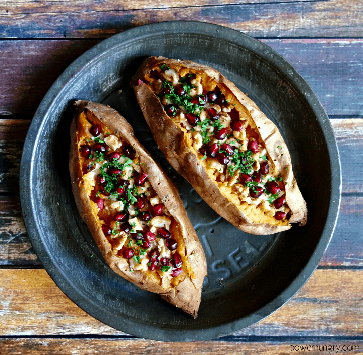 overhead shot of vegan stuffed sweet potatoes with hummus, walnuts and pomegranate sitting in an antique pie tin