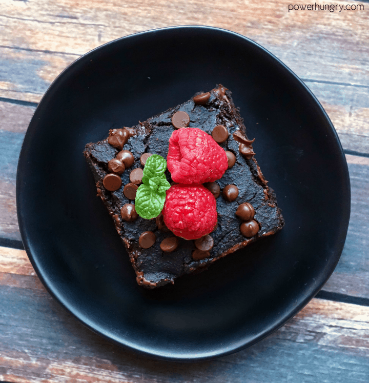overhead shot of healthy vegan breakfast blender brownie on a black plate with two raspberries on top