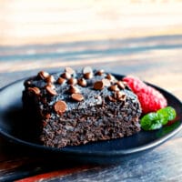 vegan breakfast brownie on a black plate, with raspberries and a mint sprig alongside