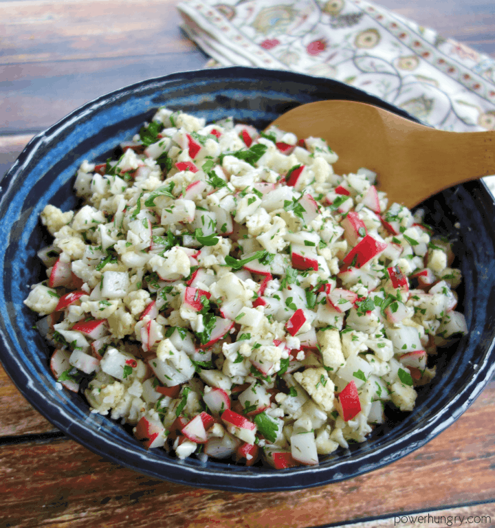  radish cauliflower salad in a blue and black pottery bowl with a wooden spoon