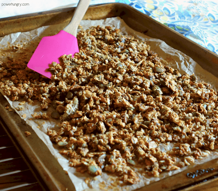 grain-free banana granola on a parchment paper-lined baking sheet with a pink silicone spatula