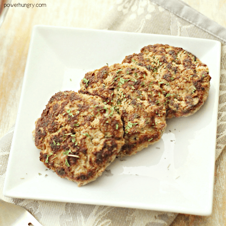 three vegan breakfast sausage patties on a white plate, topped with a sprinkle of herbs