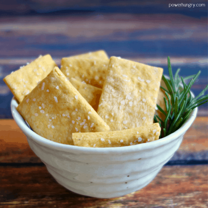 white bowl filled with vegan cheese chickpea flour crackers and a sprig of rosemary