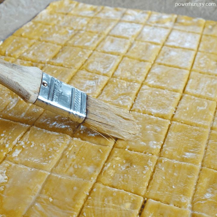 unbaked cheese-y chickpea flour crackers being brushed with water