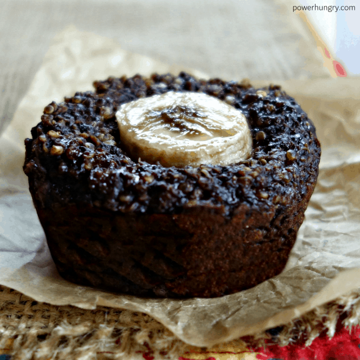 close up of one chocolate quinoa muffin, topped with a slice of banana, on a piece of parchment paper