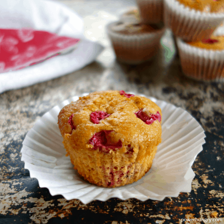 an unwrapped cranberry orange muffin atop a white muffin liner
