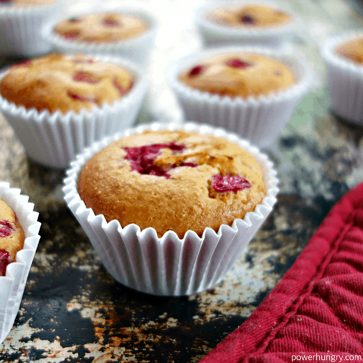 close up of a cranberry orange muffin, with more muffins and a red oven mitt close by