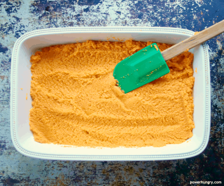 Unbaked vegan carrot soufflé being spread with a green spatula in a cream-colored serving dish