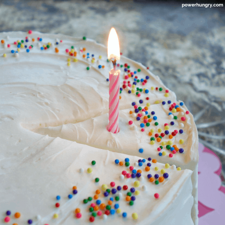 close-up of vegan and grain-free vanilla layers cake, frosted, with sprinkles and a birthday candle