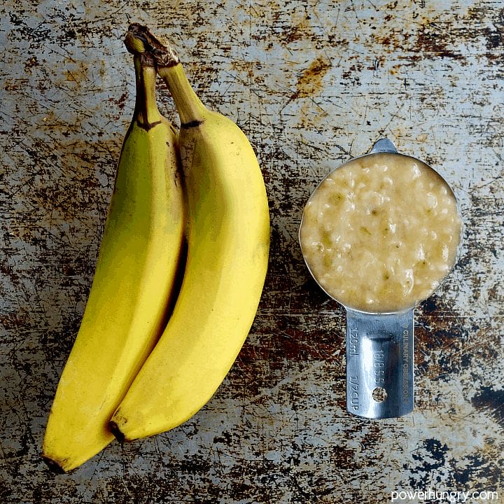 an under-ripe banana next to mashed banana in a measuring cup