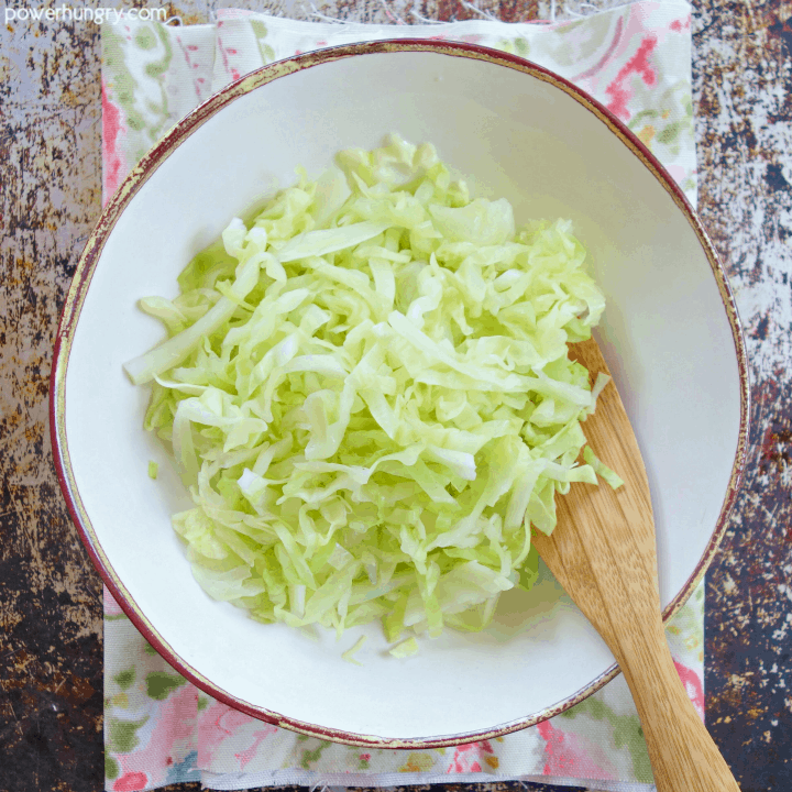 overhead shot of steamed cabbage noodles in a white bowl with a wooden spoon