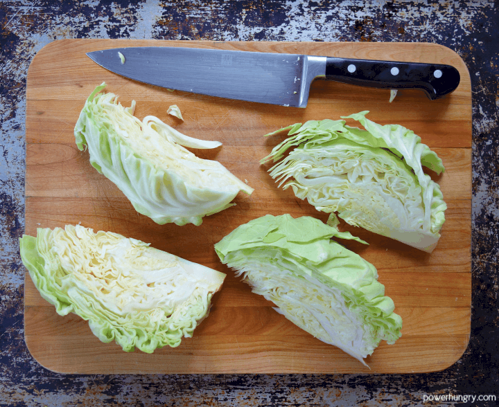 a quartered head of green cabbage on a wooden cutting board