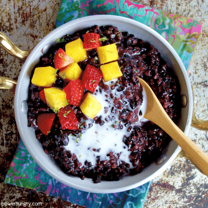 overhead shot of coconut black rice pudding in a silver and gold dish, all atop a colorful napkin