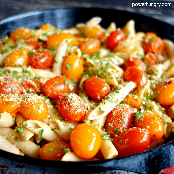 Up-close photo of cherry tomato chickpea pasta in a cast iron skillet with vegan parmesan cheese and parsley.