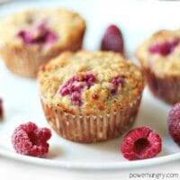 3 vegan raspberry almond flour muffins on a white plate with raspberries