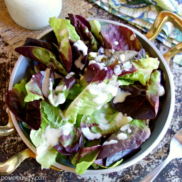 Metal bowl with gold handles filled with mixed baby lettuce and topped with a cashew based oil-free vinaigrette