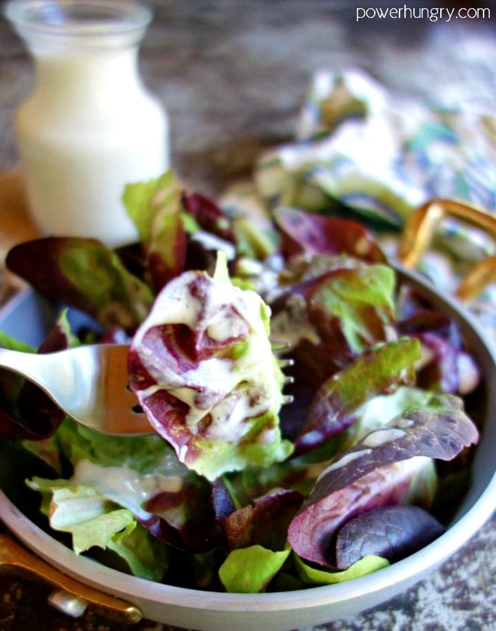 Cashew salad dressing drizzled over mixed baby lettuce in a metal dish