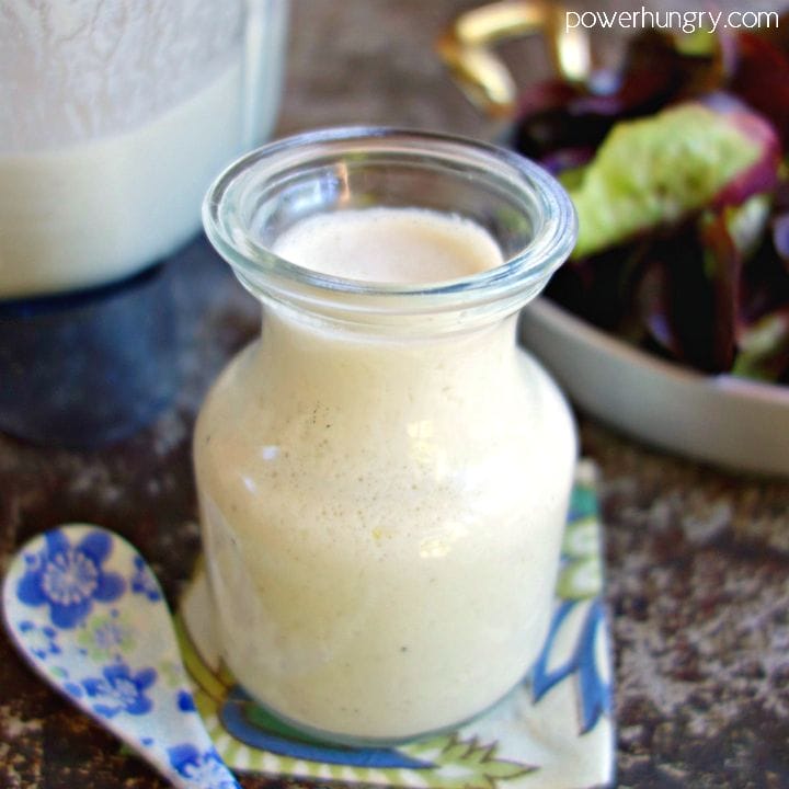 Glass bottle filled with creamy cashew dressing. Salad is in the background in a metal dish.