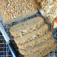 sunflower seed bread on a metal cooling rack with a bread knife and floral napkin alongside