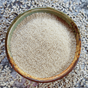 DIY sunflower seed flour in an earth-tone pottery bowl, surrounded by shelled, raw sunflower seed kernels
