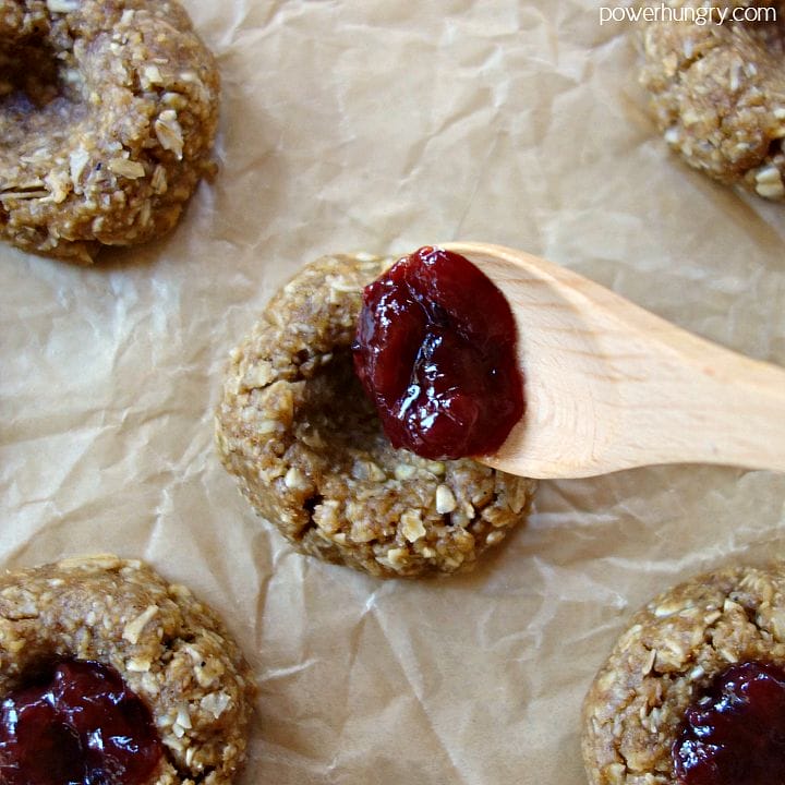 unbaked oat thumbprints being filed with jam from a wooden spoon