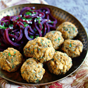yellow split pea meatballs on a hammered metal plate with beet noodles alongside