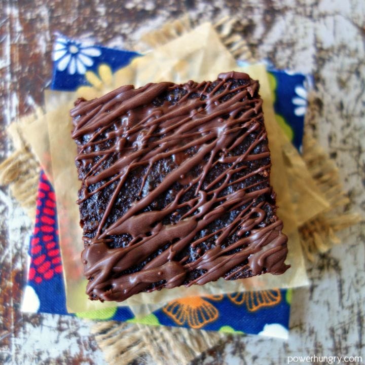 overhead shot of a brownie drizzled with dark chocolate, sitting on top of a parchment covered floral napkin