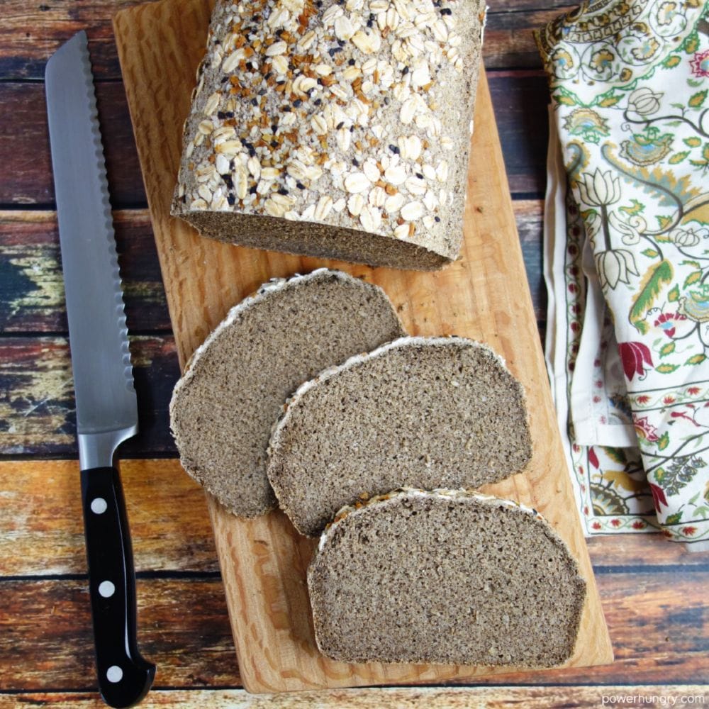 a sliced loaf of gluten-free bluckwheat bread on an artisan wood cutting board.