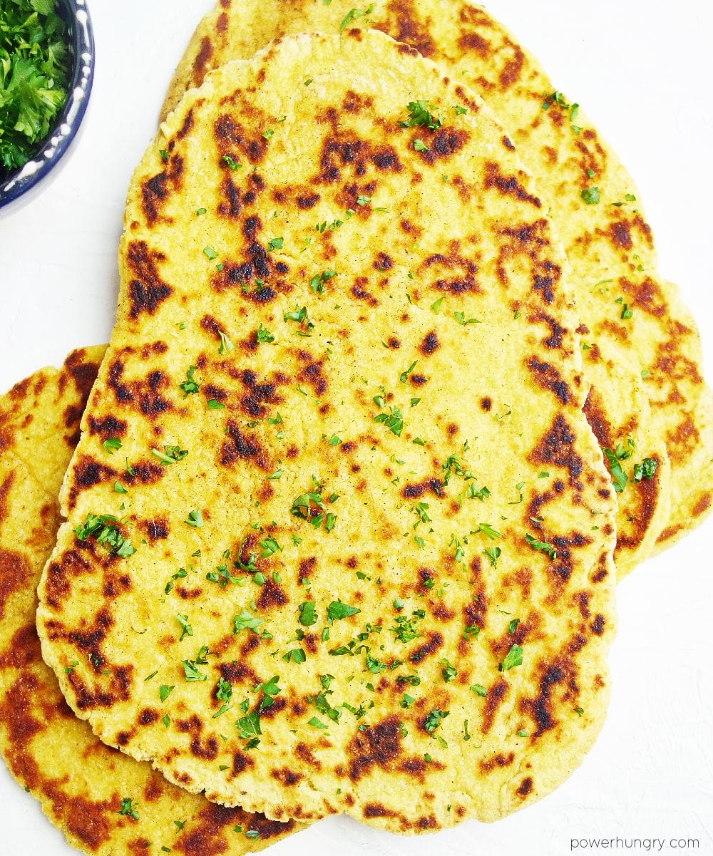 overhead shot of chickpea flour naan with a small bowl of chopped parsely leaves