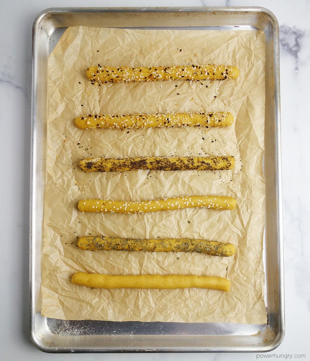unbaked chickpea flour dough ropes, rolled in seeds and herbs, on a parchment paper lined baking sheet