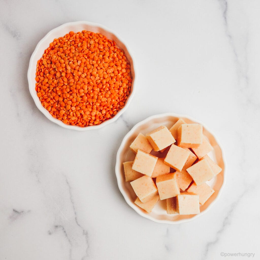 two white bowls on a marble countertop, one filled with red lentils and the other with red lentil tofu