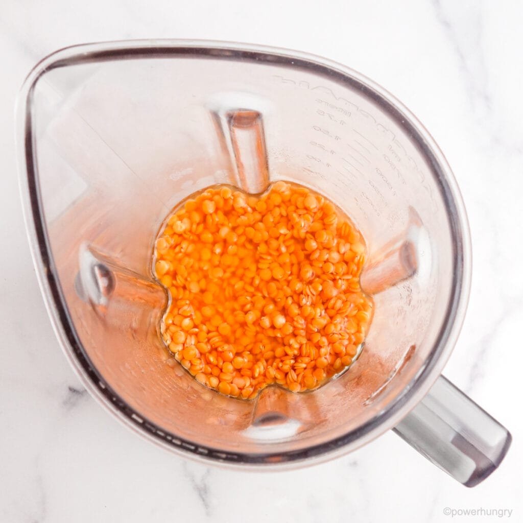 a blender container filled with soaked, plumped red lentils