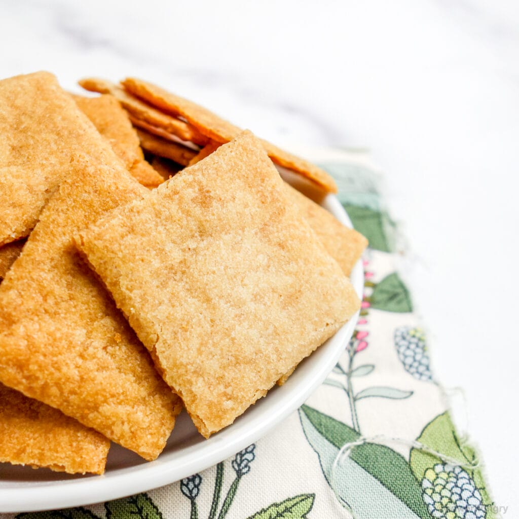 close up of cassava flour crackers in a white dish atop a floral napkin