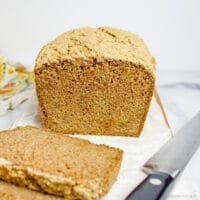 loaf of gluten-free vegan multigrain bread, sliced part way, on a cutting board